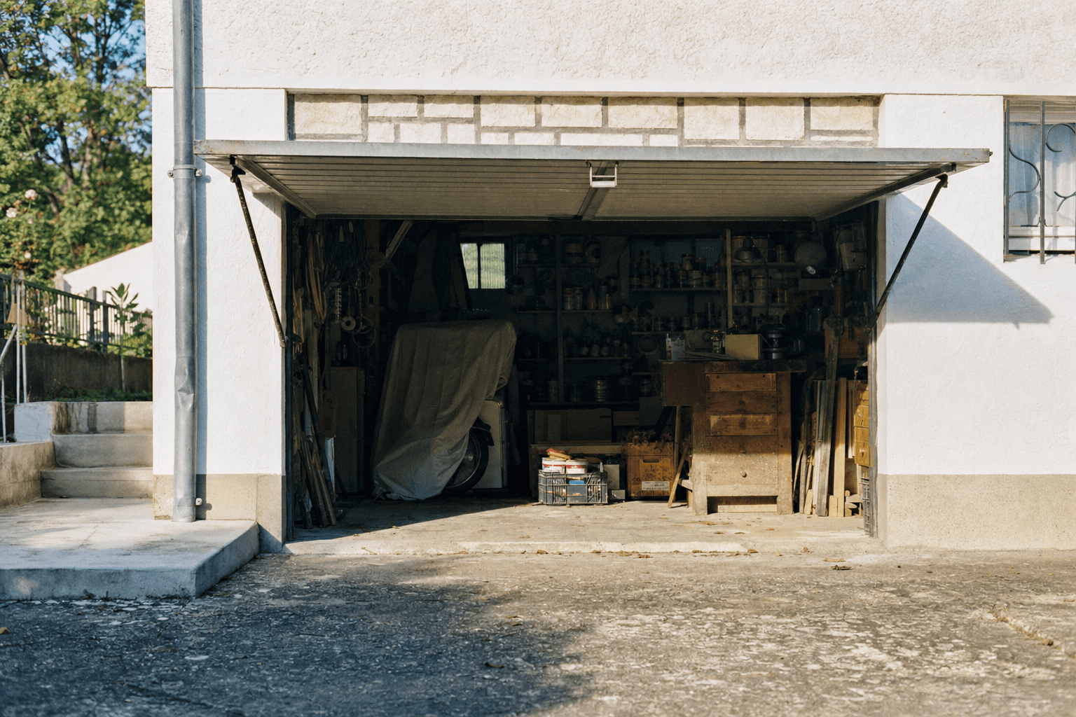 Garage de pavillon rempli d'objets accumulés, porte basculante ouverte sur la rue